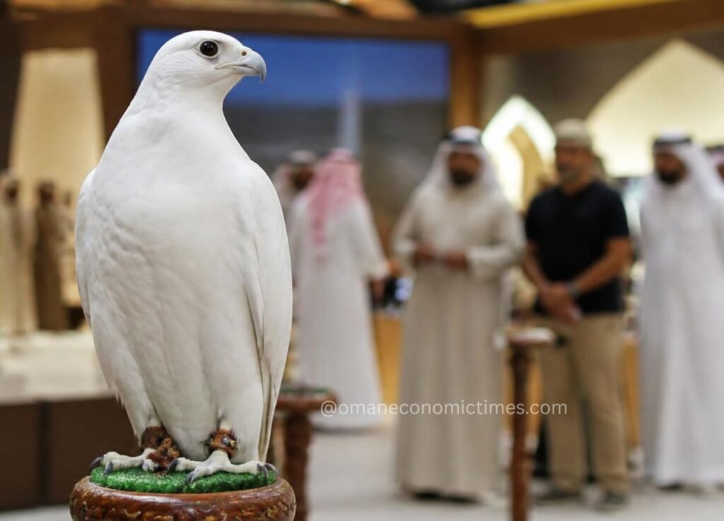Close-up of a white falcon perched on a wooden stand, with blurred attendees in traditional attire in the background.