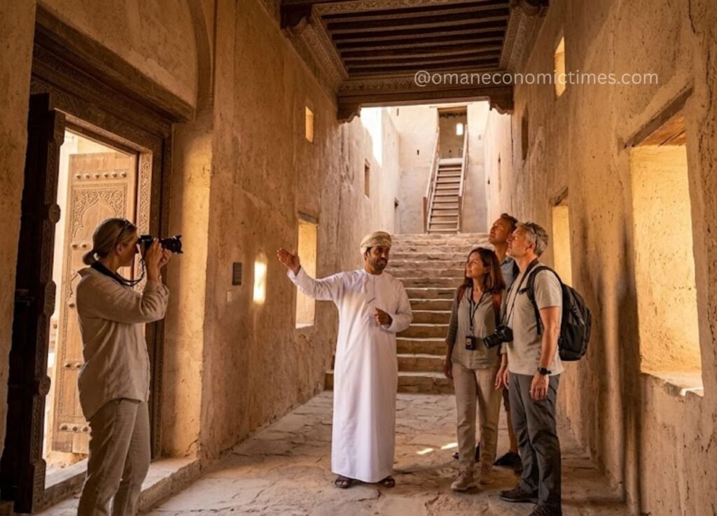 34 - Oman Economic Times Tour guide in white robes explains a historical site to three visitors with cameras inside a stone-walled corridor.
